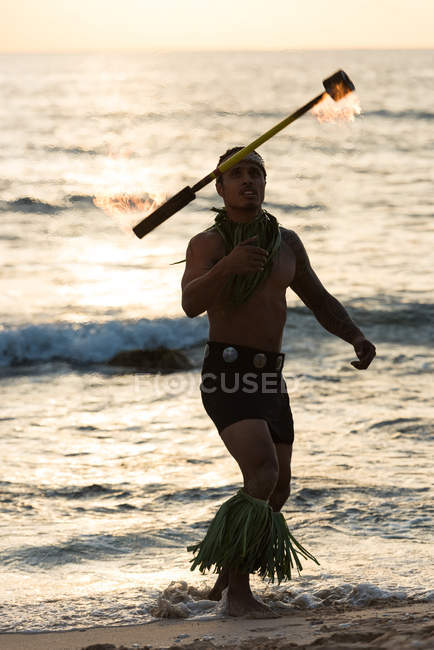 Bailarina de fuego macho girando fuego ardiente levi palo en la playa al atardecer - foto de stock