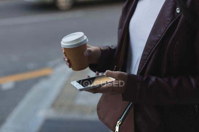 Frau benutzt Handy beim Kaffeetrinken in Stadtstraße — Stockfoto
