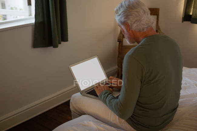 Senior man using laptop in bedroom at home — Stock Photo