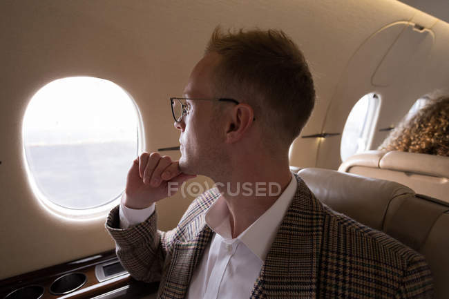Продуманий бізнесмен, дивлячись крізь вікно під час подорожі в приватному літаку — стокове фото