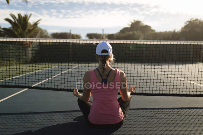 Rear view of woman performing yoga exercise in tennis court — Stock Photo
