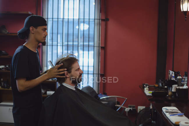 Мужчина стрижёт волосы ножницами в парикмахерской — стоковое фото