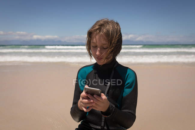 Close-up of teenage girl in wet suit using mobile phone on beach — Stock Photo
