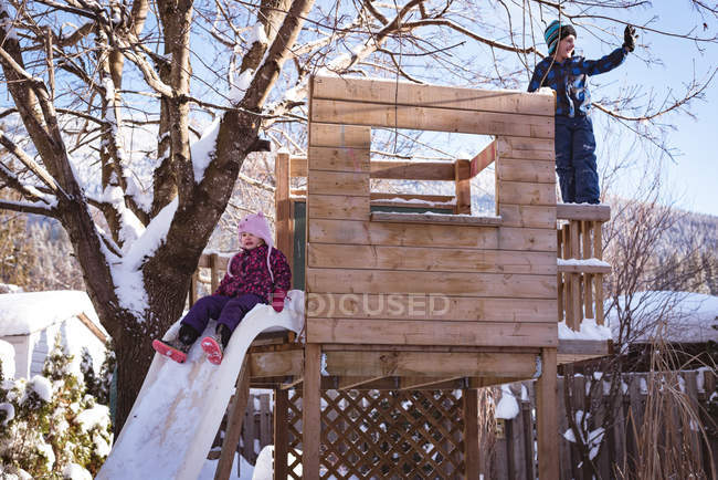 Братья и сёстры играют на заснеженной игровой площадке зимой — стоковое фото