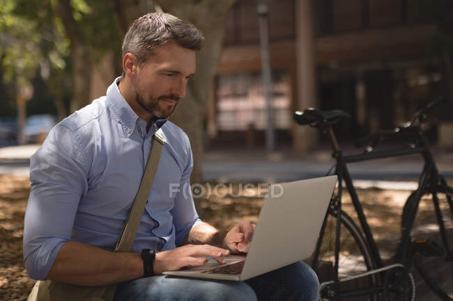 Homme utilisant un ordinateur portable dans le parc par une journée ensoleillée — Photo de stock