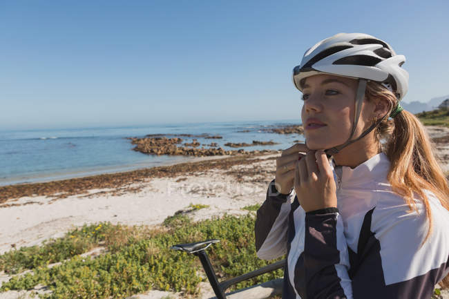 Mulher motociclista usando seu capacete perto da praia em um dia ensolarado — Fotografia de Stock