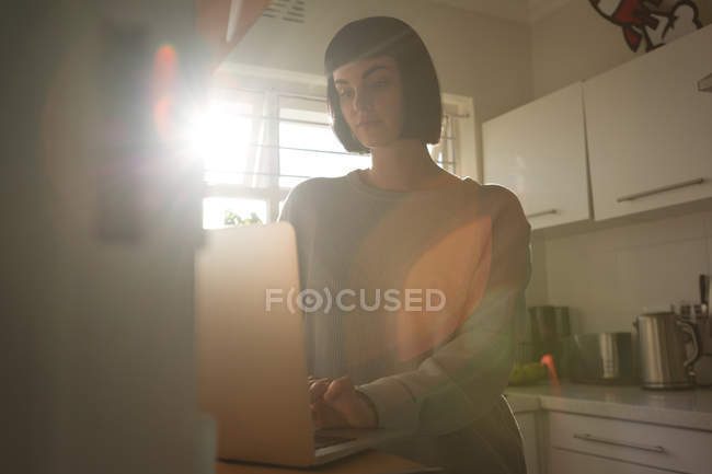Молода жінка використовує ноутбук на кухні вдома — стокове фото