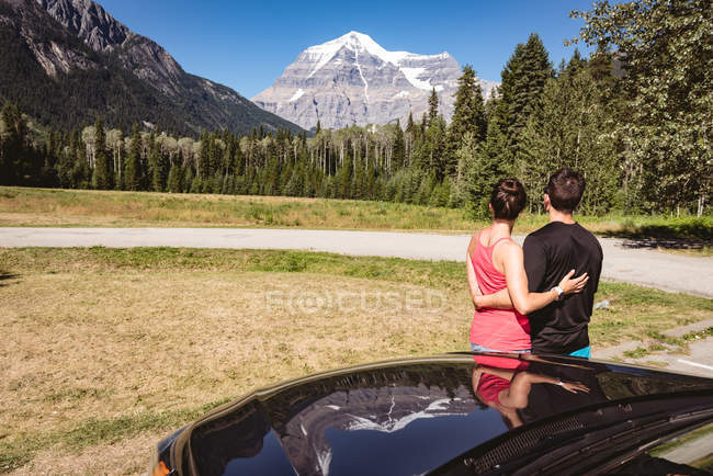 Casal olhando para montanhas cobertas de neve em um dia ensolarado — Fotografia de Stock