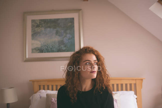 Mujer pensativa sentada en la cama en el dormitorio en casa - foto de stock