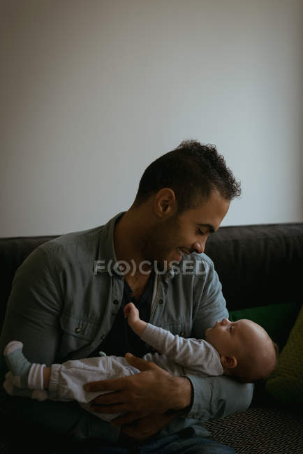 Padre sosteniendo a su bebé en la sala de estar en casa - foto de stock