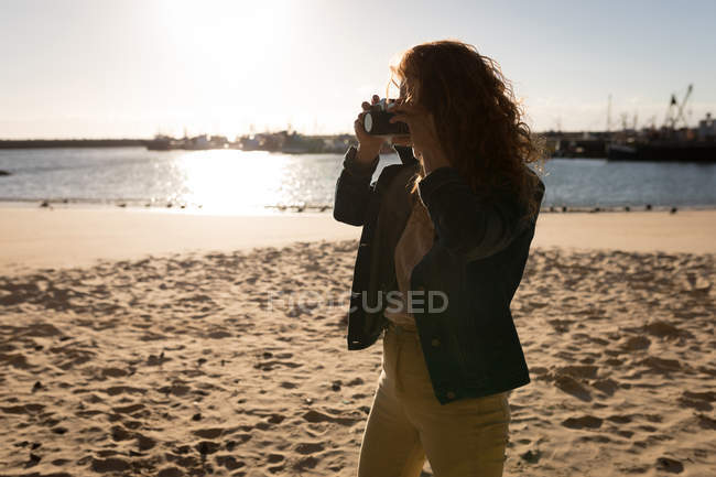 Woman taking photo with camera on beach at sunset — Stock Photo