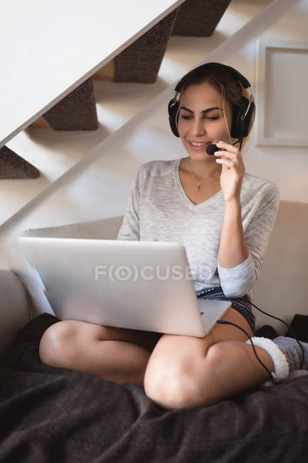 Woman using laptop with headset in living room at home — Stock Photo
