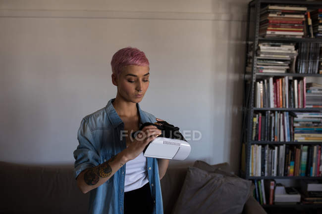 Jeune femme aux cheveux roses tenant casque de réalité virtuelle à la maison . — Photo de stock