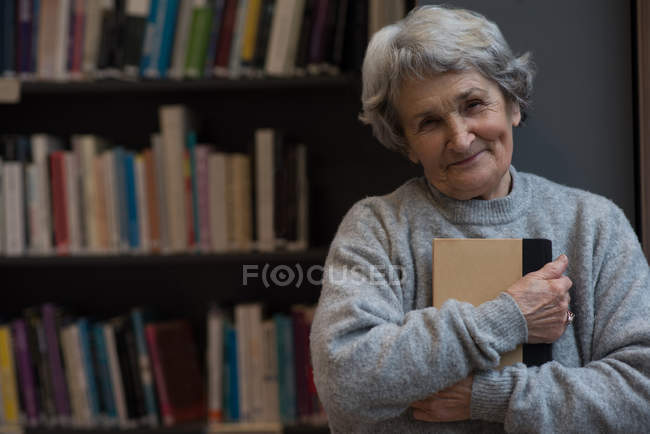Retrato de mulher idosa segurando um livro na biblioteca — Fotografia de Stock
