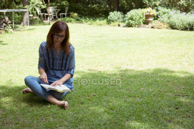 Donna che legge libro in giardino in una giornata di sole — Foto stock