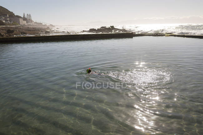 Donna che nuota nella piscina sulla spiaggia alla luce del sole — Foto stock