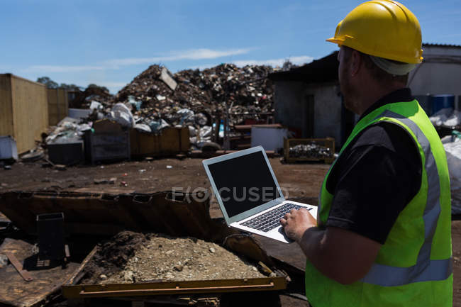 Rückansicht des Arbeiters mit seinem Laptop auf dem Schrottplatz — Stockfoto