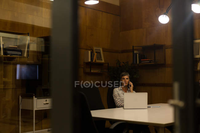 Зрелая деловая женщина разговаривает по мобильному телефону в офисе — стоковое фото