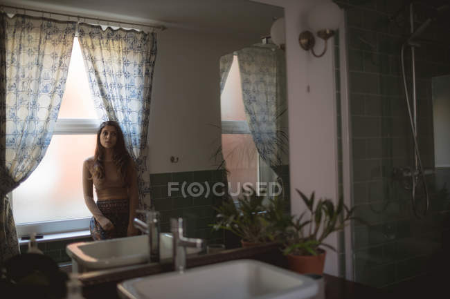 Задумчивая женщина сидит на подоконнике в ванной комнате — стоковое фото