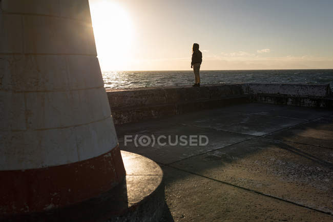 Femme observant le paysage marin près du phare pendant le coucher du soleil — Photo de stock