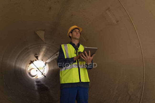 Trabalhador masculino usando tablet digital enquanto examina um túnel de concreto na estação solar — Fotografia de Stock