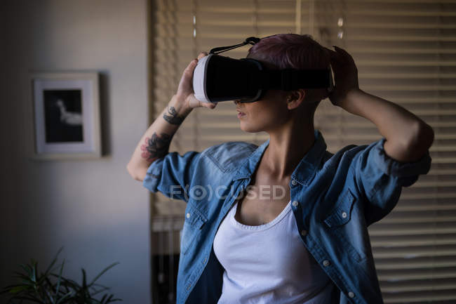 Mujer joven usando auriculares de realidad virtual en casa. - foto de stock