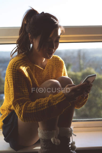 Женщина с мобильного телефона возле окна дома — стоковое фото