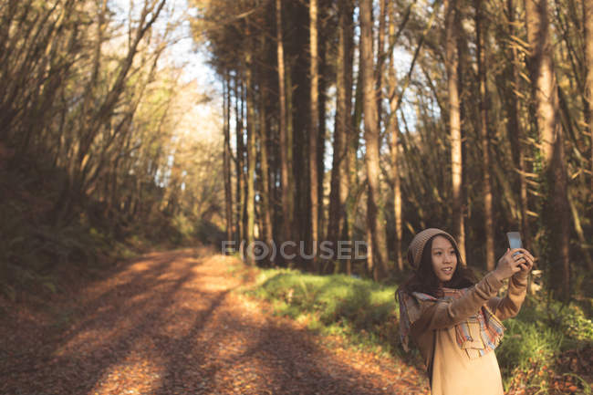 Женщина делает селфи с мобильного телефона в лесу — стоковое фото