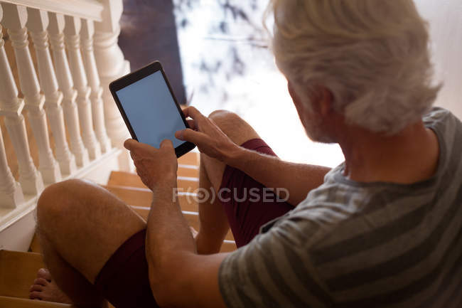 Homem sênior usando tablet digital nas escadas em casa — Fotografia de Stock