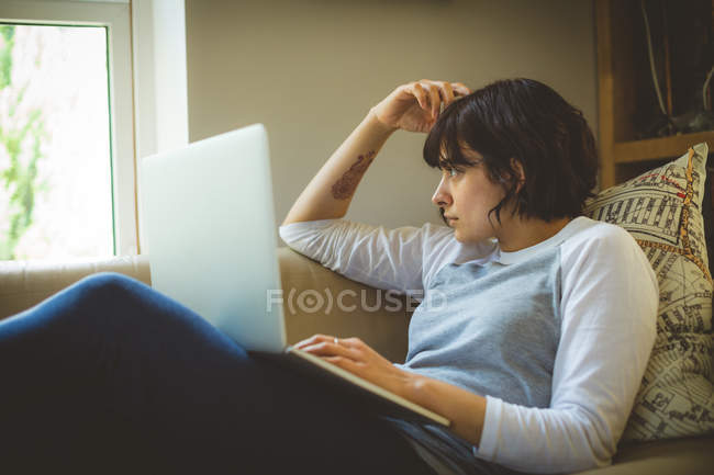 Mujer reflexiva usando el teléfono móvil en la sala de estar en casa - foto de stock