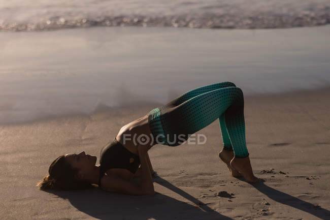 Fitte Frau beim Yoga in der Abenddämmerung am Strand. — Stockfoto