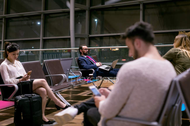 Commuters using electronic devices in waiting room at airport — Stock Photo