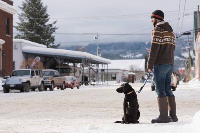Man standing with dog on sidewalk during winter. — Stock Photo