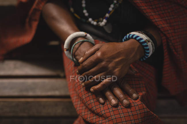 Sección media del hombre maasai con ropa tradicional sentado en el banco - foto de stock