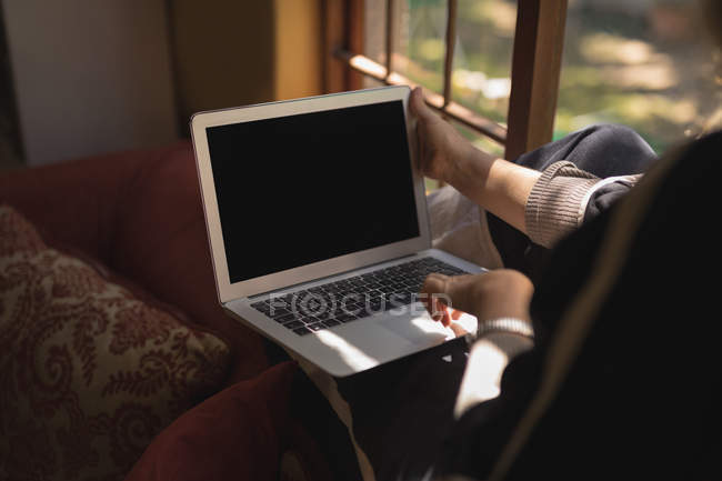 Sección media de la mujer madura usando el ordenador portátil en la sala de estar - foto de stock