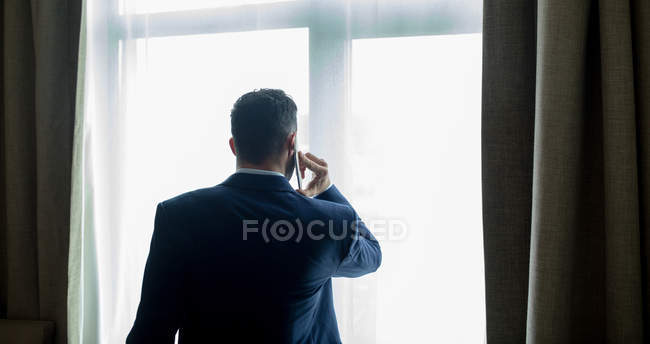Rear view of businessman talking on mobile phone in hotel room — Stock Photo