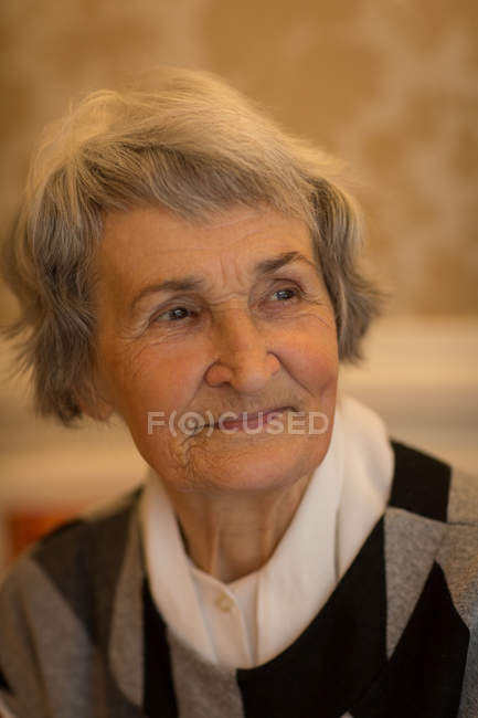 Задумчивая пожилая женщина улыбается дома — стоковое фото