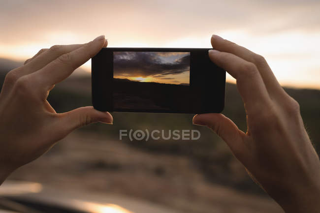 Mulher tirando foto da natureza com telefone celular ao pôr do sol — Fotografia de Stock