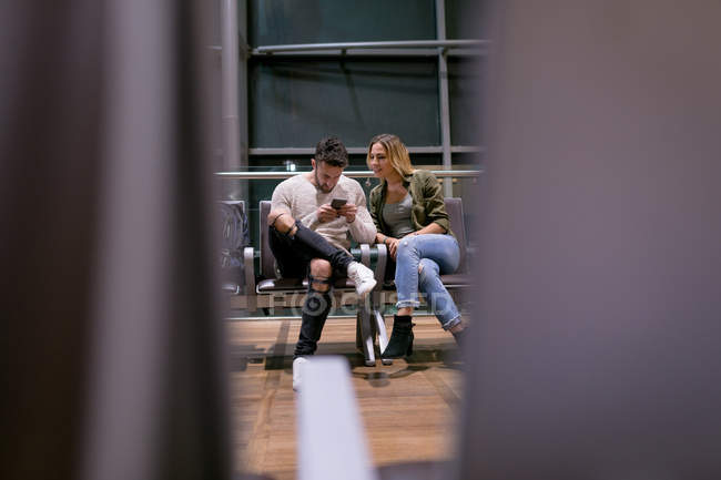 Pareja usando teléfono móvil en la sala de espera en el aeropuerto - foto de stock