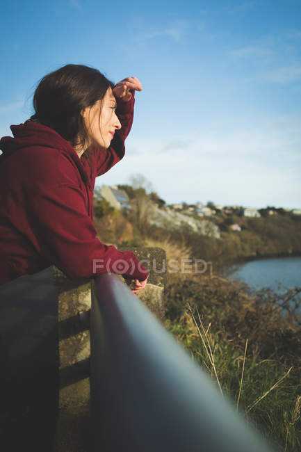 Frau steht und lehnt an Geländer am Flussufer. — Stockfoto