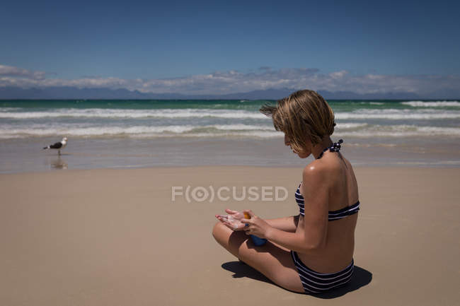 Ragazza adolescente che applica crema solare lozione sul retro in spiaggia — Foto stock