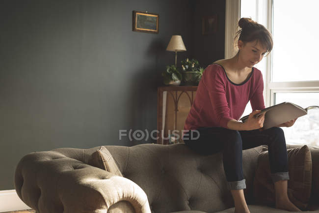 Mujer leyendo libro en la sala de estar en casa - foto de stock