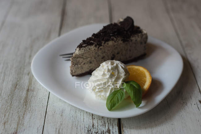 Delicious cake with whipped cream, lemon slice and mint in plate on wooden table — Stock Photo