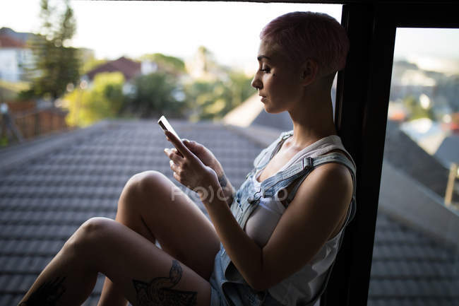 Stilvolle Frau nutzt Handy am Fenster zu Hause. — Stockfoto