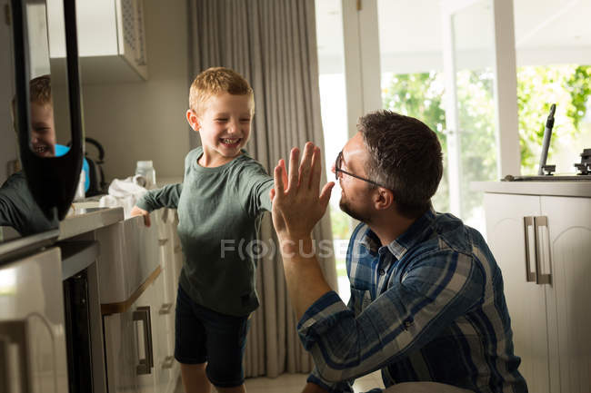 Padre e hijo dando choca los cinco unos a otros en la cocina en casa - foto de stock