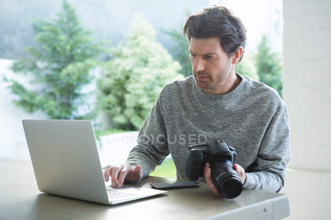Человек с ноутбуком и с цифровой камерой дома — стоковое фото