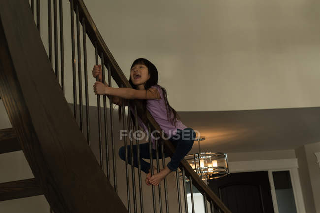 Happy girl playing on staircase railing at home — Stock Photo