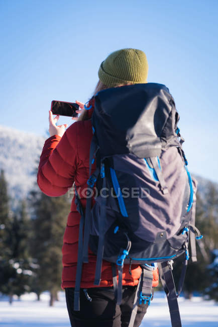 Mulher clicando em uma imagem no telefone inteligente durante o inverno — Fotografia de Stock