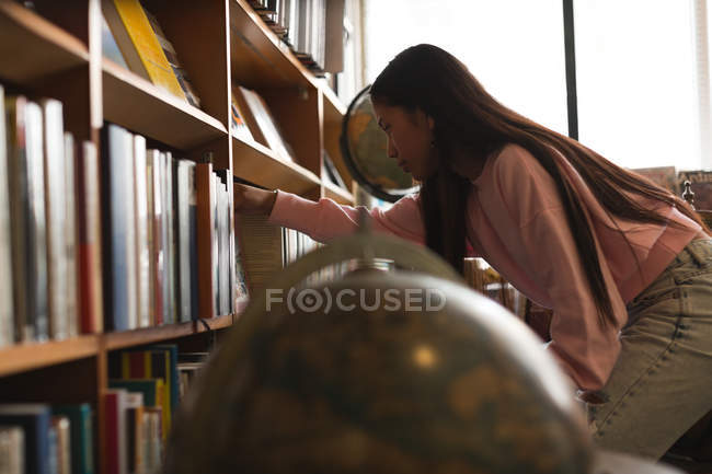 Vista lateral da adolescente selecionando um livro na biblioteca — Fotografia de Stock