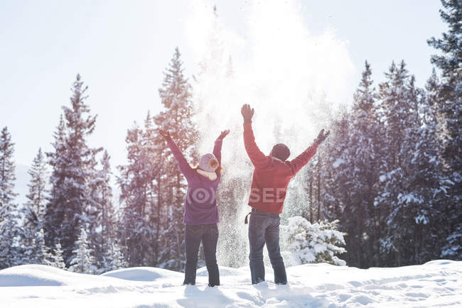 Paar wirft Schnee in die Luft im verschneiten Wald in den Bergen. — Stockfoto